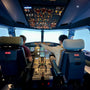Two people operating a realistic commercial flight simulator cockpit with illuminated panels.